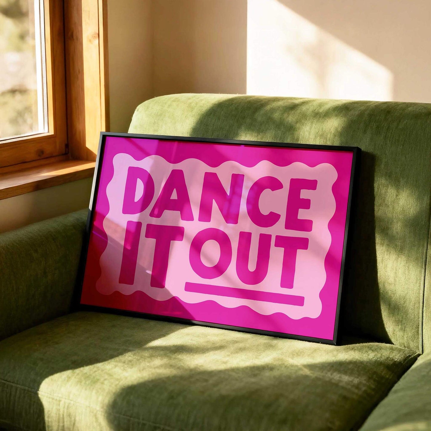 A framed poster with the text "DANCE IT OUT" in pink and white colors is displayed on a green couch.