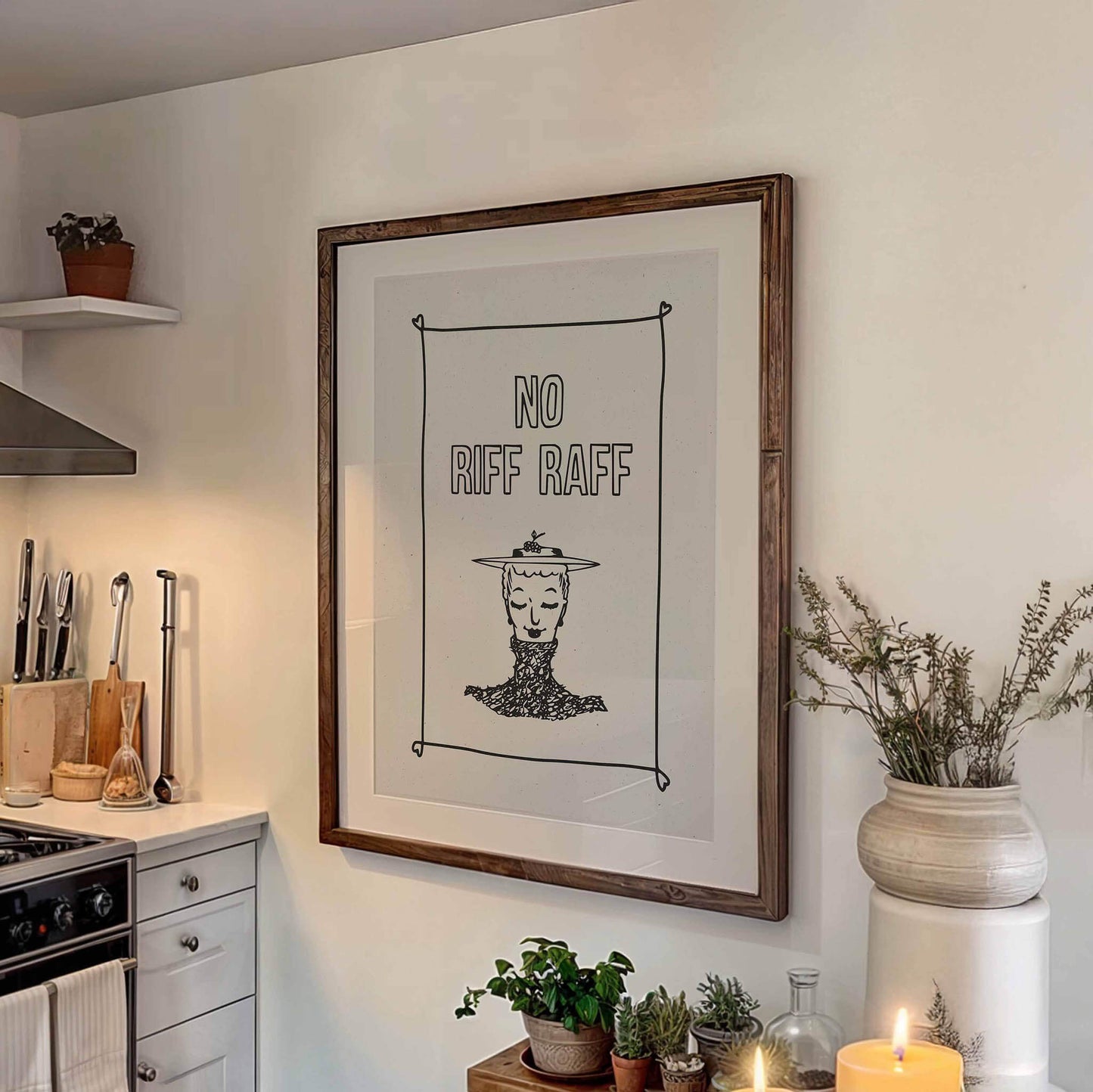 a framed artwork hanging on a wall, depicting a woman's face with the text "NO RIFF RAFF" above it. The artwork is surrounded by various kitchen items, including a potted plant, a vase, and a set of knives.