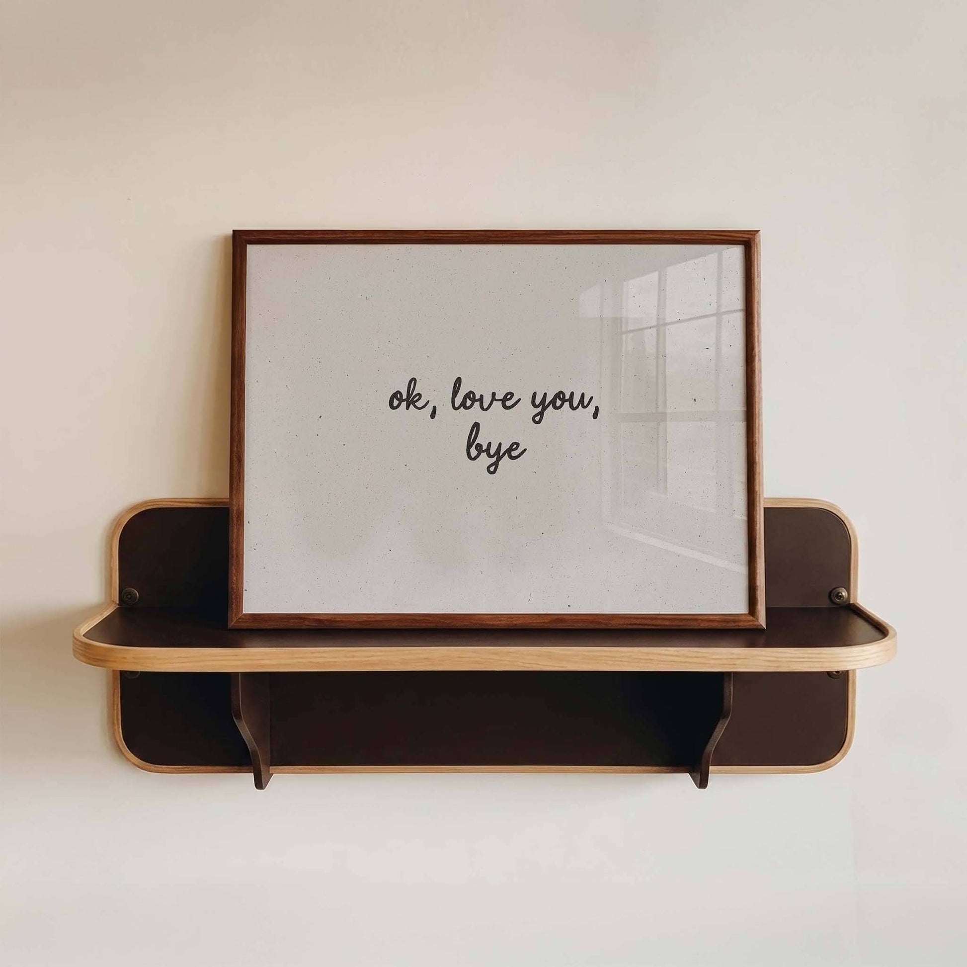 Wooden shelf with a framed picture displaying 'ok, love you, bye' on a white wall.