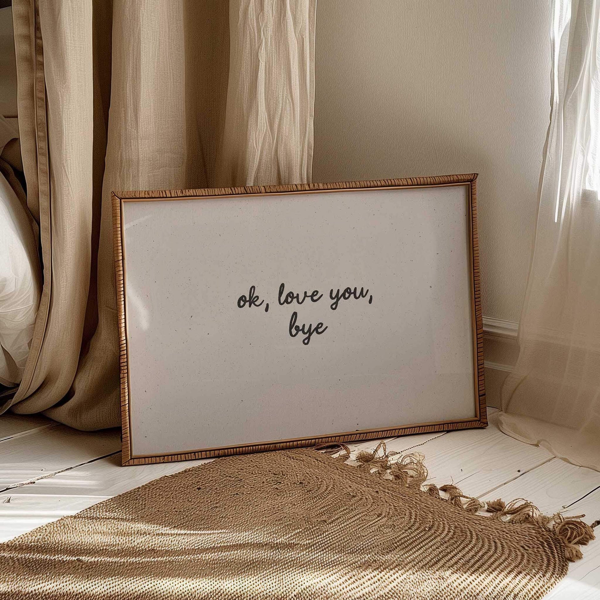 Framed artwork with 'ok, love you, bye' text on a wooden floor with curtains in the background