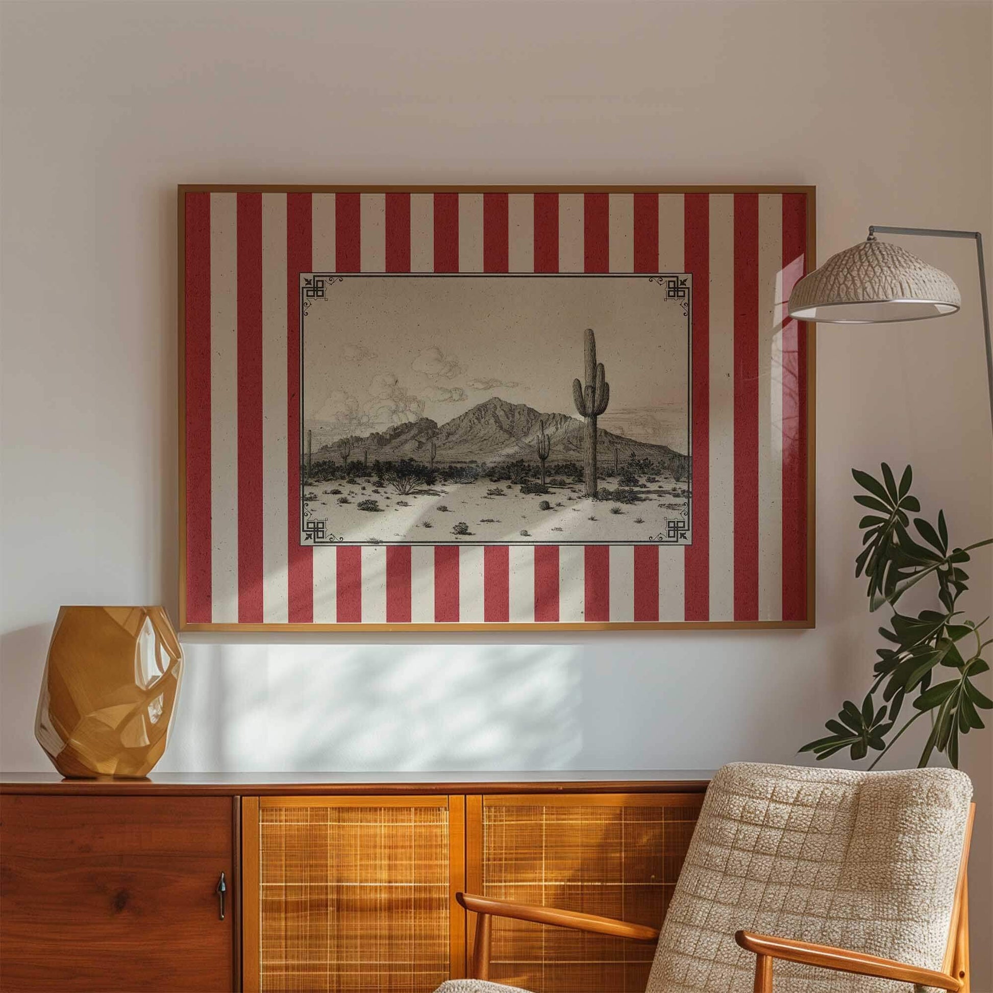 a framed picture of a desert landscape with a cactus in the center, hanging on a wall above a wooden cabinet.