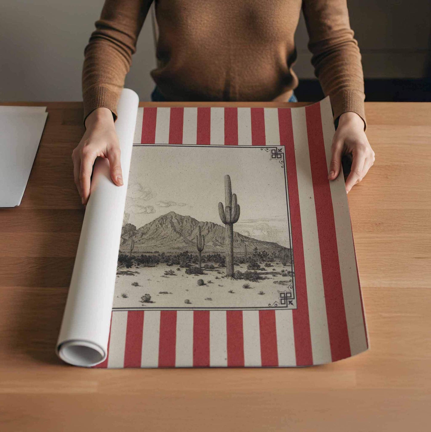 A person is holding a large piece of paper with a desert landscape printed on it, which features a cactus and mountains in the background.
