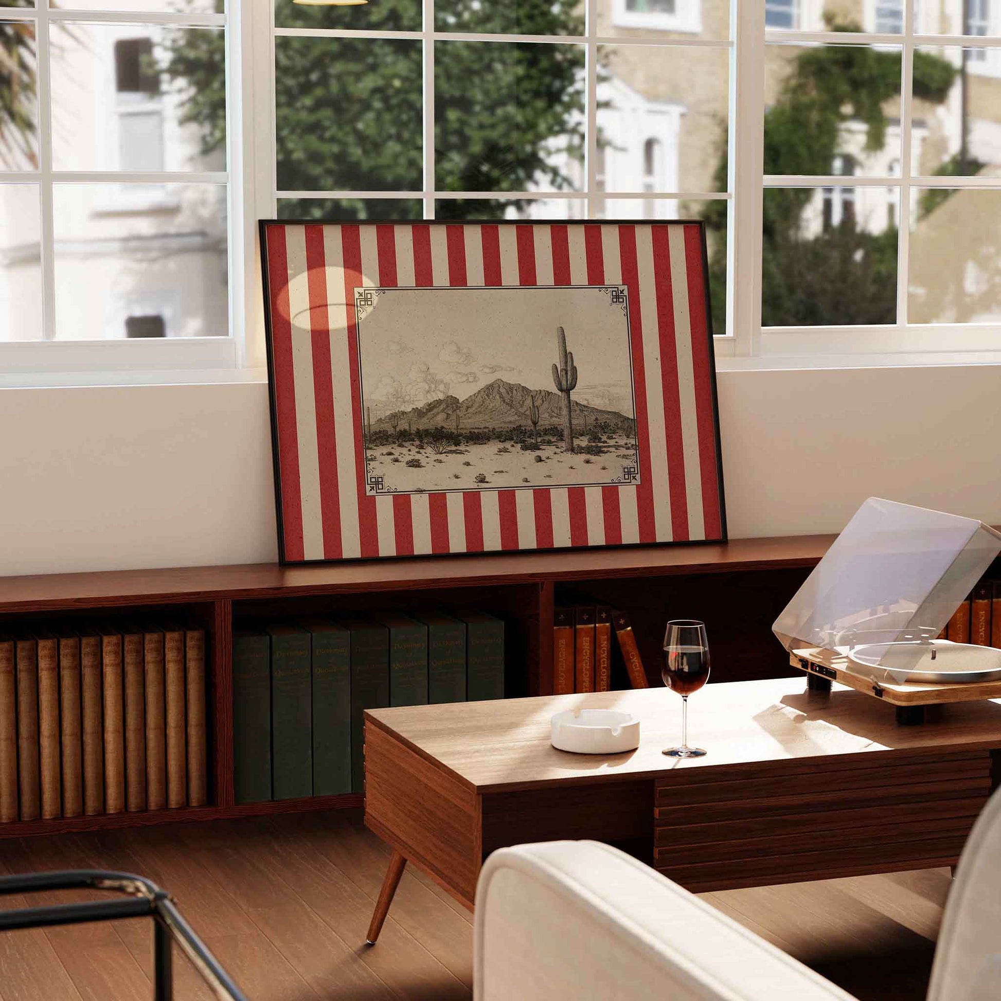 a framed desert landscape artwork on a wooden shelf, with a glass of red wine on a wooden table in front of it.