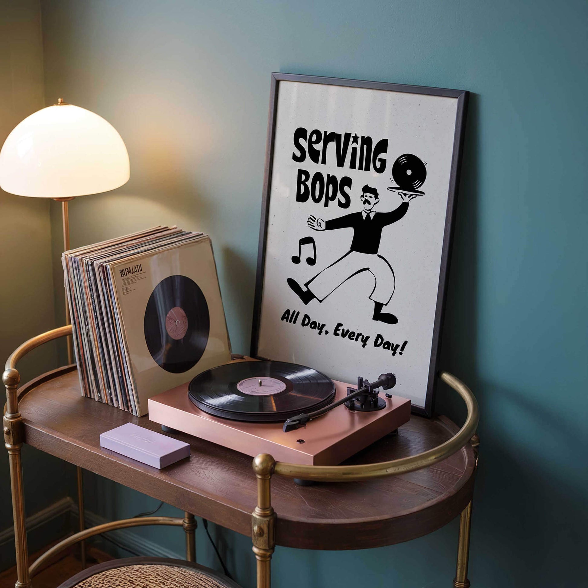 a turntable with a record album, a framed poster with a cartoon character, and a lamp on a wooden table.