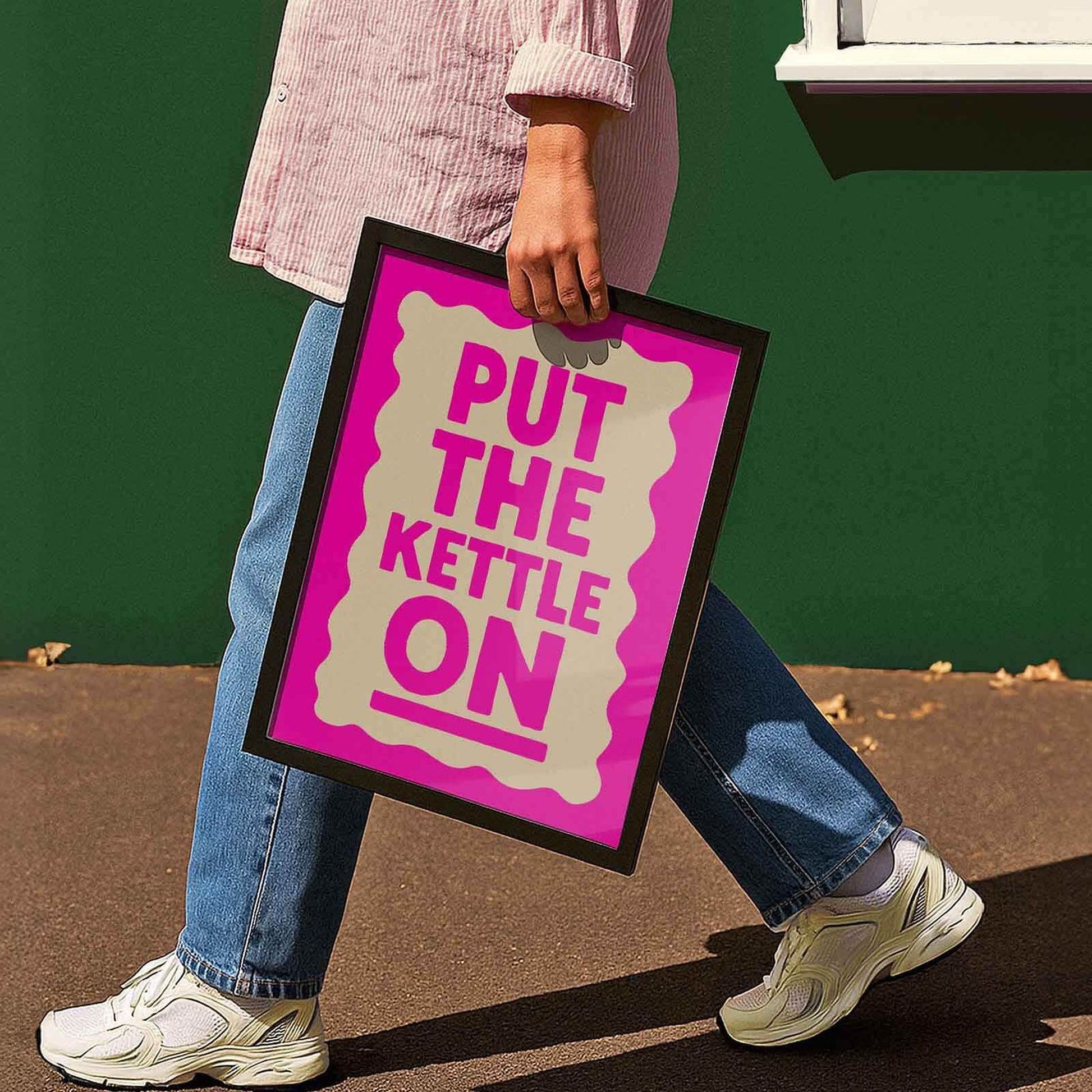 A person is walking while holding a sign that says "PUT THE KETTLE ON".