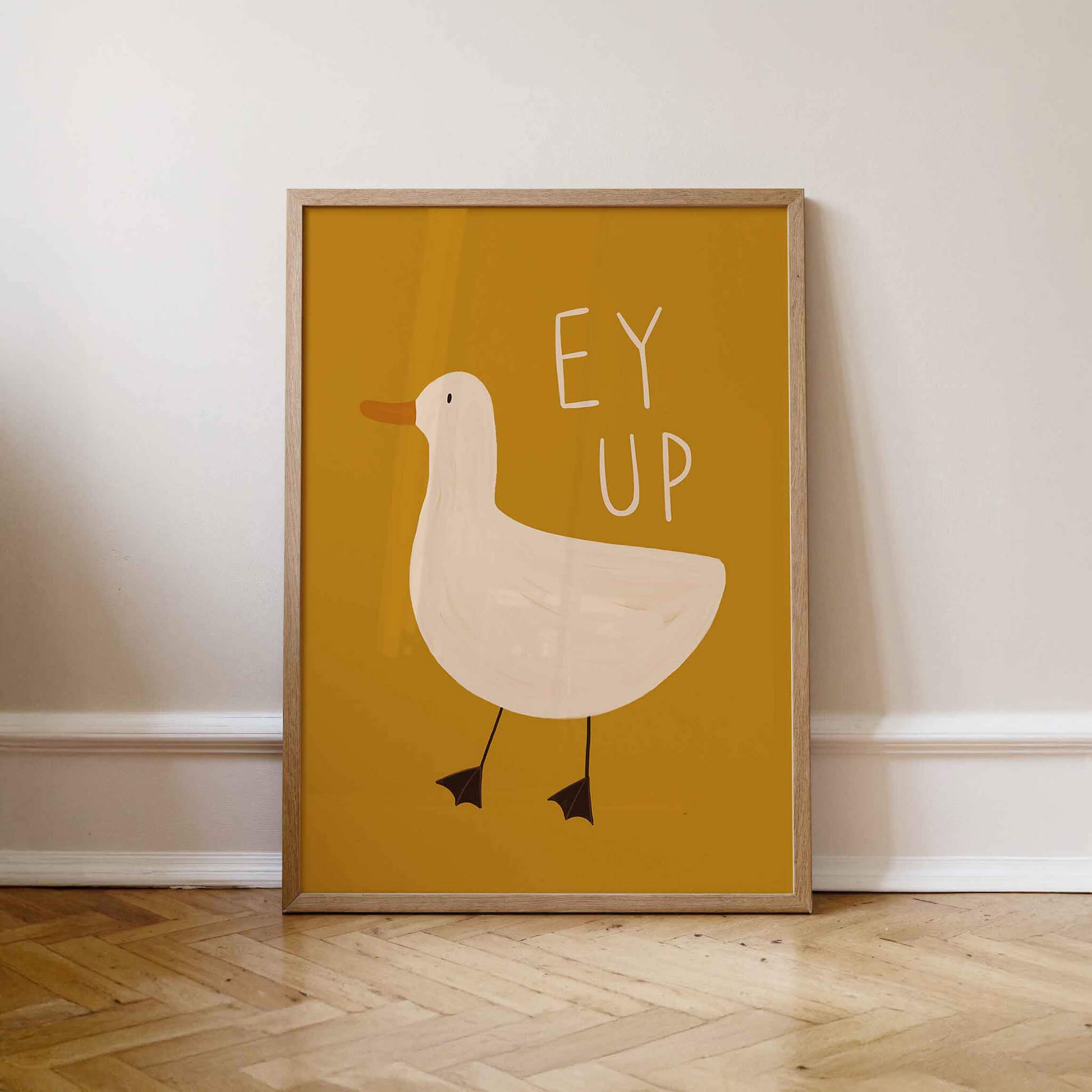 Framed Yorkshire themed wall art with a mustard yellow background and duck illustration and 'EY UP' text. Leaning against a wall.